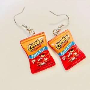 May include: A pair of drop earrings featuring miniature replicas of Cheetos Party Size snack bags. The charms are orange and red with the Cheetos logo and the text Party Size! printed in blue. Each charm hangs from a silver-toned metal hook.