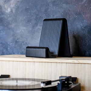 May include: A black record player stand with a black phone stand on top. The stand is made of wood and has a light wood finish. The background is a dark blue with white stars.