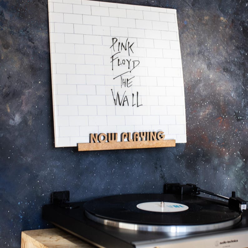 May include: A white vinyl record with the text "Pink Floyd The Wall" on the cover. A turntable is playing the record. A wooden sign above the turntable reads "Now Playing".