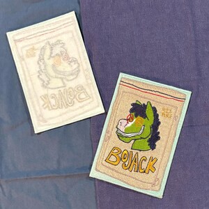 May include: Two embroidered patches featuring a cartoon horse character. One patch is a light beige color with a green horse head, sunglasses, and the word "BOJACK" in yellow. The other patch is a lighter version of the same design.