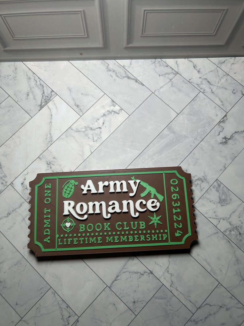 Może przedstawiać: Brązowy i zielony znak w kształcie biletu. Na znaku widnieje napis "Army Romance Book Club Lifetime Membership" białymi literami. Znak ma zieloną obw&oacute;dkę i przedstawia granat i karabin.