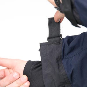 May include: A black jacket with a black strap and velcro closure on the cuff. The jacket has a navy blue section on the lower arm.