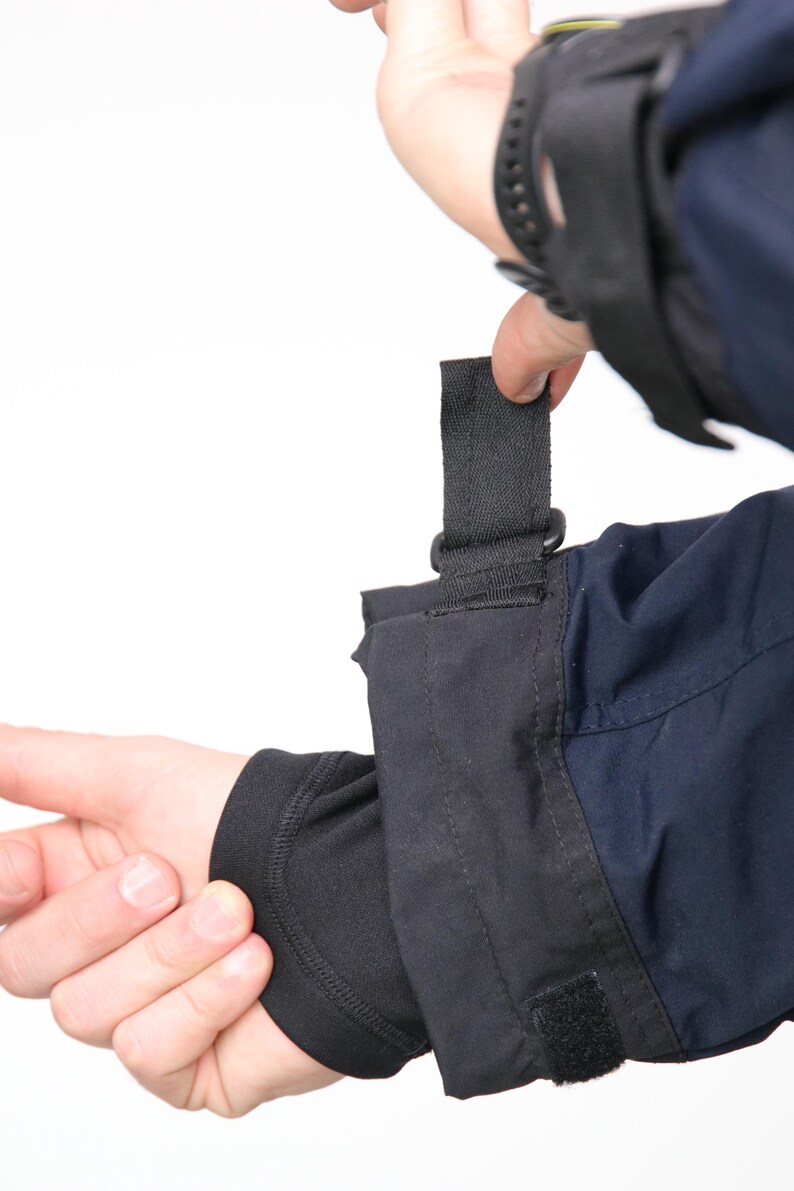 May include: A black jacket with a black strap and velcro closure on the cuff. The jacket has a navy blue section on the lower arm.