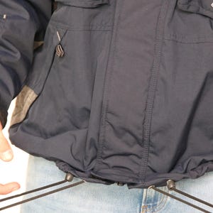 May include: A navy blue jacket with a drawstring waist and two pockets on the front. The jacket has a zipper closure and a hood.
