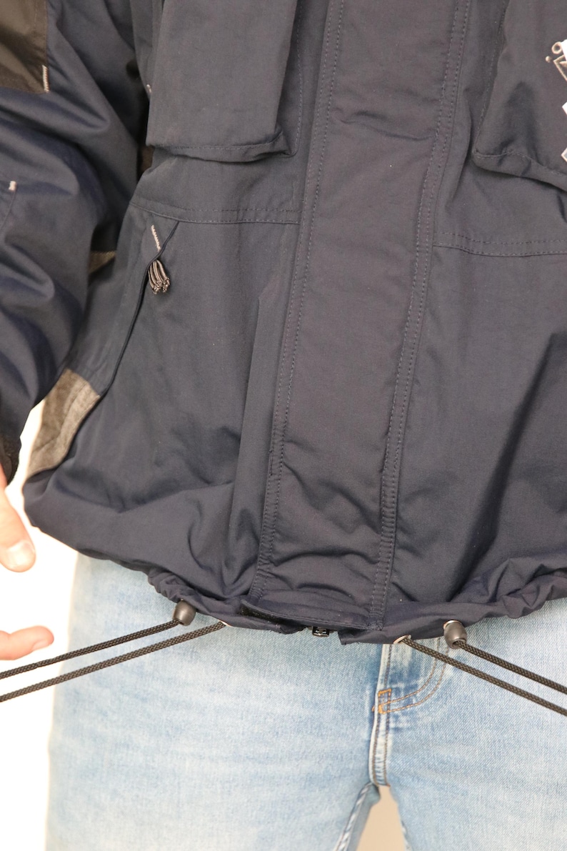 May include: A navy blue jacket with a drawstring waist and two pockets on the front. The jacket has a zipper closure and a hood.