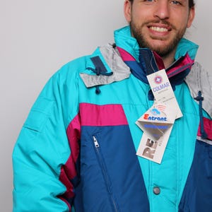 Op de afbeelding: Een turquoise, blauwe, roze en grijze ski-jas met een Colmar Sportwear logo-label. De jas heeft een ritssluiting en een knoopsluiting.