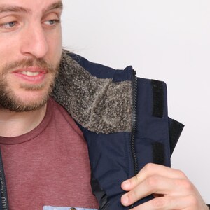 May include: A navy blue jacket with a black zipper and a fleece lining. The jacket has a velcro strap on the left side of the collar. The text "SYSTEM CO. MAR. OVERSYST" is visible on the left side of the jacket.