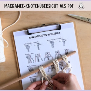 Peut inclure: Une feuille de papier blanche avec un presse-papiers noir sur le dessus. Le papier porte un titre qui se lit "Makramee-Knotenübersicht als PDF" et une liste de différents nœuds de macramé avec des illustrations et des instructions. Les nœuds comprennent "Ankerknoten vorwärts", "Kreuzknoten", "Wellenknoten", et "Rippenknoten".