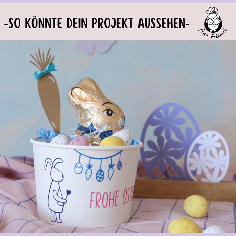 Puede incluir: Un vaso de papel blanco con un dise&ntilde;o de conejo y el texto "Frohe Ostern" (Feliz Pascua) est&aacute; lleno de huevos de chocolate, un conejito de chocolate y una zanahoria de papel marr&oacute;n con una cinta azul. El vaso est&aacute; sobre un mantel a cuadros rosa y blanco.
