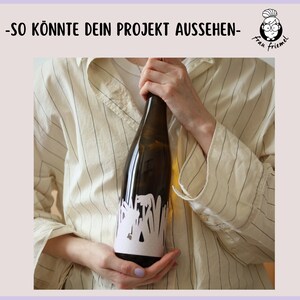 Pu&ograve; includere: Una persona tiene in mano una bottiglia di vino bianco con un'etichetta bianca che presenta un disegno floreale. L'etichetta riporta il testo "Frau Friemmel".