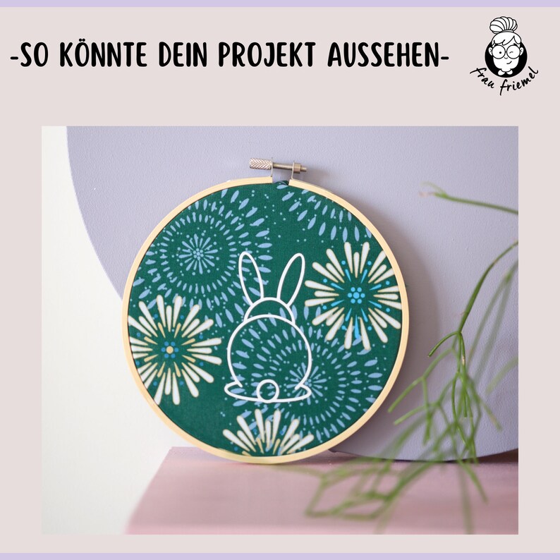 K&ouml;nnte beinhalten: Ein gr&uuml;ner Stickrahmen mit einer wei&szlig;en Umrandung eines Kaninchens auf einem gr&uuml;n-blauen Blumenmuster.
