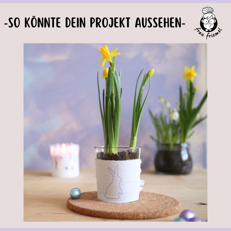 K&ouml;nnte beinhalten: Eine Glasvase mit einem wei&szlig;en Papierband, das mit einer lila Hasensilhouette verziert ist. Die Vase ist mit Erde gef&uuml;llt und hat zwei gelbe Narzissen, die darin wachsen. Die Vase steht auf einem Korkuntersetzer.