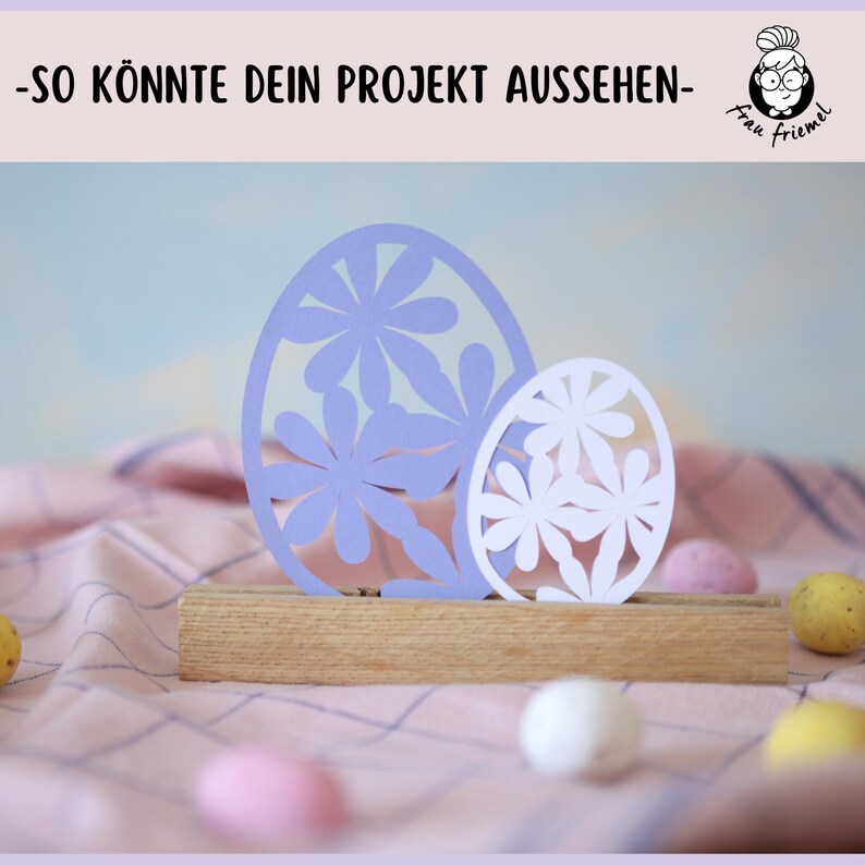Puede incluir: Dos huevos de Pascua de papel con dise&ntilde;os de flores recortados. El huevo m&aacute;s grande es morado y el m&aacute;s peque&ntilde;o es blanco. Los huevos se muestran en un soporte de madera.