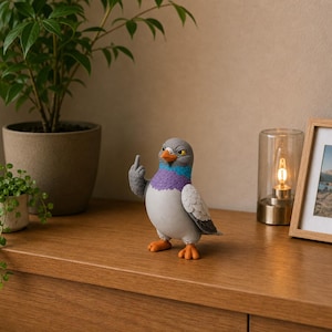 Colorful pigeon decoration displayed on a wooden cabinet beside green plants, framed artwork and a warm lamp, featuring textured grey wings.