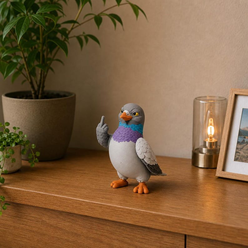 Colorful pigeon decoration displayed on a wooden cabinet beside green plants, framed artwork and a warm lamp, featuring textured grey wings.