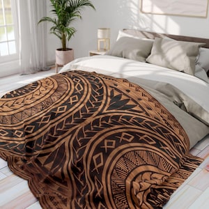 Op de afbeelding: Een bruin en zwart patroon deken met een tribaal ontwerp is over een bed gedrapeerd. De deken heeft geometrische vormen en gebogen lijnen. Het bed heeft witte en grijze beddengoed, en de kamer heeft een plant en een raam.