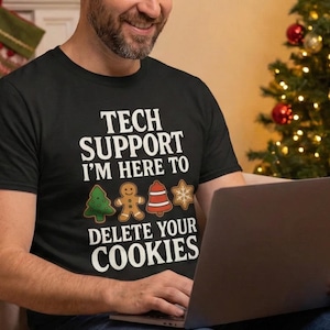 Peut inclure: Un t-shirt noir avec le texte "TECH SUPPORT I'M HERE TO DELETE YOUR COOKIES" et des graphiques de biscuits de Noël. La personne est assise sur un canapé avec une assiette de biscuits et un ordinateur portable. Un sapin de Noël est en arrière-plan.