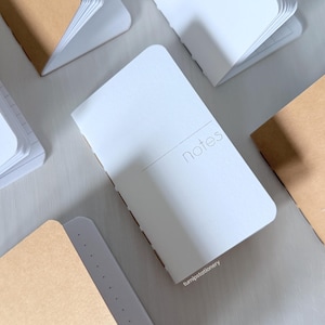May include: A collection of small notebooks with brown and white covers. The notebooks have the word "notes" printed on the front.