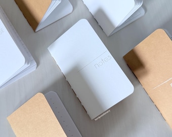 May include: A collection of small notebooks with brown and white covers. The notebooks have the word "notes" printed on the front.
