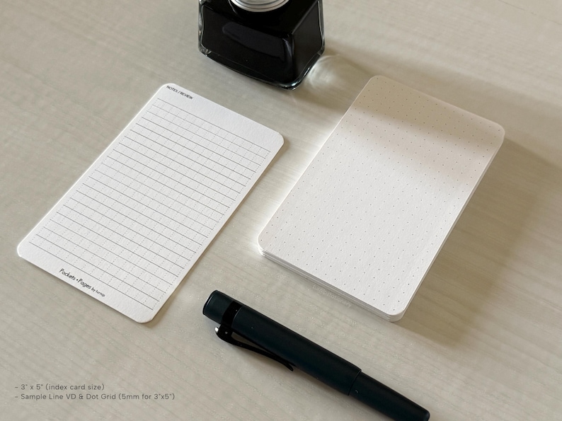 A side view of a set of index card-sized, note cards on a white table. The card on the left has a line with mini vertical dots layout with the text "Pockets + Pages by Turnip" at the bottom. The stack of cards on the right has a dot grid layout. A black ink bottle and small blue pen is placed nearby.