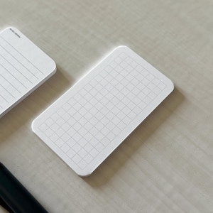 A side view of a set of business card-sized graph cards on a white table, next to a small stack of line note cards. A small blue pen is placed nearby.