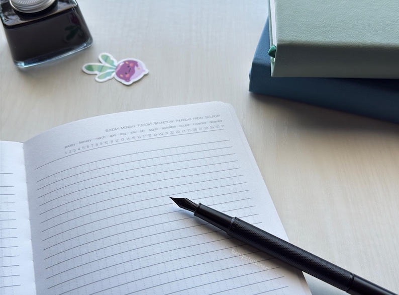 An open notebook showing a clean, structured layout using solid lines with vertical dots, featuring an undated days, months, and weeks calendar at the top. Two PU-leather notebooks with green and blue covers are stacked nearby on a white desk. There is a black fountain pen on top of the notebook and an ink bottle and a small turnip sticker nearby.