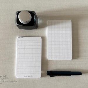 A set of index card-sized note cards on a white table. The card on the left has a line with mini vertical dots layout with the text "Pockets + Pages by Turnip" at the bottom. The stack of cards on the right has a graph layout. A black ink bottle and small blue pen is placed nearby.
