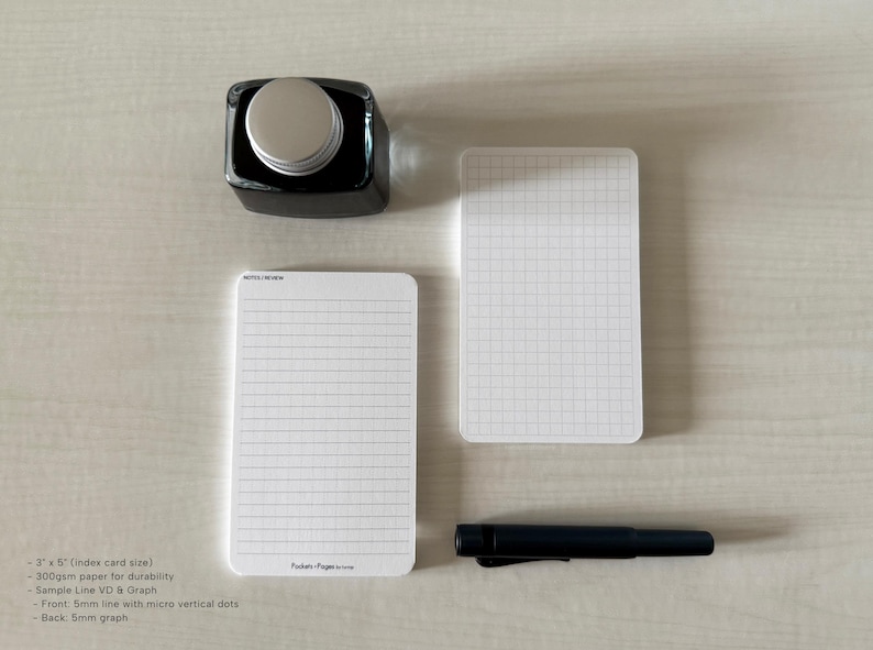 A set of index card-sized note cards on a white table. The card on the left has a line with mini vertical dots layout with the text "Pockets + Pages by Turnip" at the bottom. The stack of cards on the right has a graph layout. A black ink bottle and small blue pen is placed nearby.