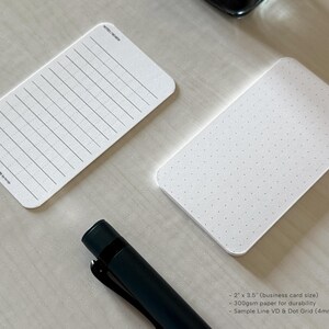 A side view of a set of business card-sized, note cards on a white table. The card on the left has a line with mini vertical dots layout with the text "Pockets + Pages by Turnip" at the bottom. The stack of cards on the right has a dot grid layout. A black ink bottle and small blue pen is placed nearby.