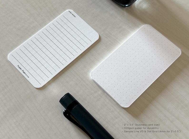 A side view of a set of business card-sized, note cards on a white table. The card on the left has a line with mini vertical dots layout with the text "Pockets + Pages by Turnip" at the bottom. The stack of cards on the right has a dot grid layout. A black ink bottle and small blue pen is placed nearby.