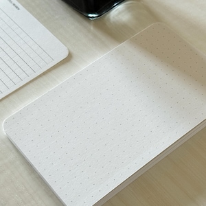 A focus view of a set of index card-sized note cards on a white table. The card on the left has a line with mini vertical dots layout with the text "Notes/Review" at the top left of the card. The stack of cards on the right has a dot grid layout. The dot grid card is focused in to show the mini dots. A black ink bottle and small pen is placed nearby.