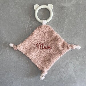 Op de afbeelding: Een roze pluche baby speelgoed met een witte bijtring. Het speelgoed is geborduurd met de naam "Mavi".