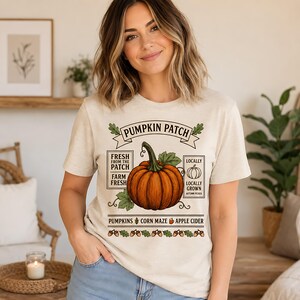 Könnte beinhalten: Ein cremefarbenes T-Shirt mit einem Grafikdruck mit dem Text PUMPKIN PATCH, FRESH FROM THE PATCH, FARM FRESH, LOCALLY GROWN und AUTUMN PICKED. Das Design enthält einen großen orangefarbenen Kürbis, Blätter sowie Text für PUMPKINS, CORN MAZE und APPLE CIDER.