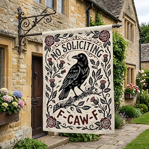 Könnte beinhalten: Eine cremefarbene Outdoor-Flagge mit einem schwarzen Raben auf einem Ast, umgeben von floralen und Distel-Designs. Die Flagge trägt die Aufschrift "NO SOLICITING" über dem Raben und "F-CAW-F" darunter. Die Flagge hängt vor einem Steingebäude.