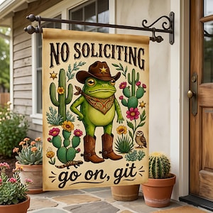 Könnte beinhalten: Eine rechteckige Gartenflagge mit einem grünen Frosch, der einen braunen Cowboyhut, ein gemustertes Halstuch und braune Cowboystiefel trägt. Die Flagge zeigt oben den Text NO SOLICITING und unten go on, git, umgeben von Kakteen.