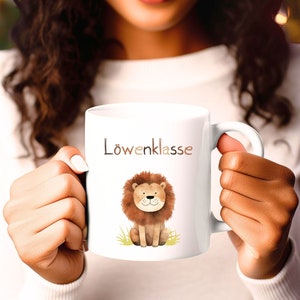 Könnte beinhalten: Weiße Keramiktasse mit einer braunen Löwenillustration und dem Text "Löwenklasse" in braunen Buchstaben.