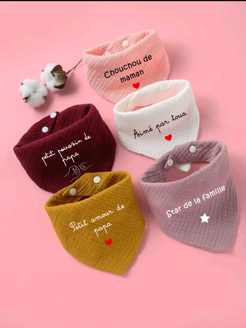 K&ouml;nnte beinhalten: F&uuml;nf Baby-L&auml;tzchen in verschiedenen Farben: Rosa, Wei&szlig;, Burgunderrot, Gelb und Lavendel. Jedes L&auml;tzchen hat einen franz&ouml;sischen Text und einen Druckknopfverschluss. Auf rosa Hintergrund.