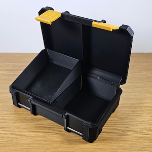 May include: A black plastic storage box with a yellow latch. The box has a removable divider and is open to reveal the interior.