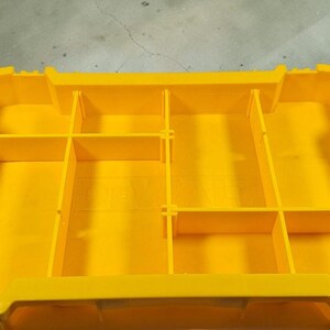 May include: A yellow tool organiser with several compartments. The organiser has a rectangular shape with dividers creating storage spaces. The interior is solid yellow, and the exterior has black accents. The dimensions are not visible.