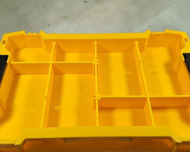 May include: A yellow tool organiser with several compartments. The organiser has a rectangular shape with dividers creating storage spaces. The interior is solid yellow, and the exterior has black accents. The dimensions are not visible.