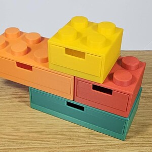 May include: A set of four colorful stackable storage drawers shaped like Lego bricks. The drawers are green, orange, red, and yellow.
