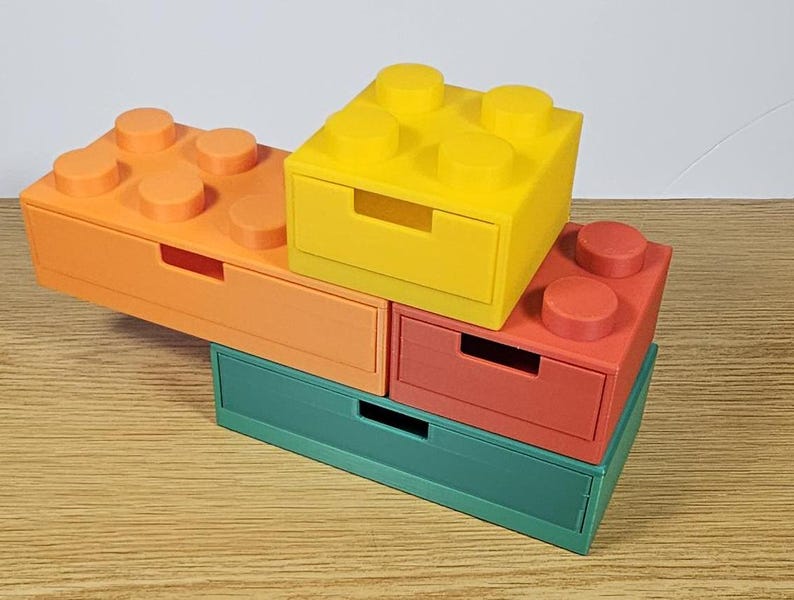 May include: A set of four colorful stackable storage drawers shaped like Lego bricks. The drawers are green, orange, red, and yellow.