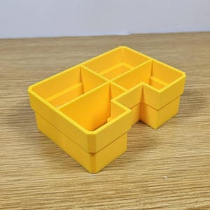 May include: A bright yellow, multi-compartment organizer. The organizer has a rectangular shape with several internal dividers, creating distinct sections. The design is simple and functional, with a clean, modern aesthetic. The organizer is made of a solid, opaque material.