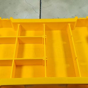 May include: A bright yellow plastic storage organiser with multiple compartments and dividers. The organiser has a rectangular shape with vertical and horizontal dividers, creating various storage spaces. The design is clean and functional, suitable for tools or small items.