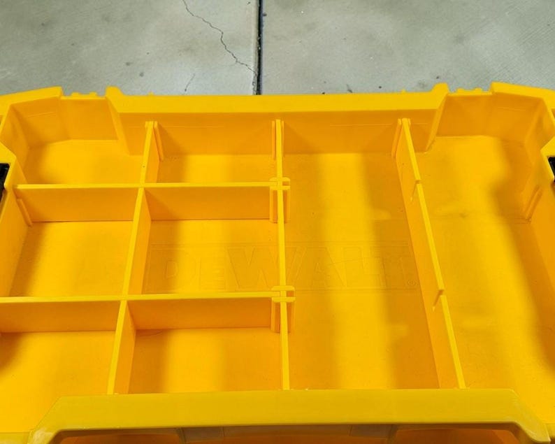May include: A bright yellow plastic storage organiser with multiple compartments and dividers. The organiser has a rectangular shape with vertical and horizontal dividers, creating various storage spaces. The design is clean and functional, suitable for tools or small items.