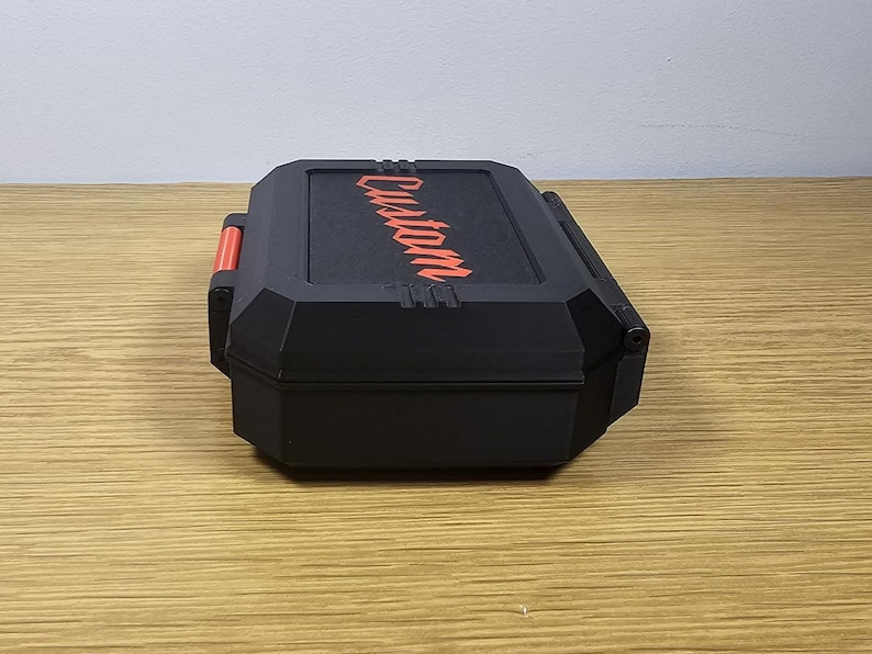 May include: Black rectangular case with the word "Custom" in red diagonally across the top. The case has a red accent on the side and is sitting on a wooden surface. The case appears to be a storage container.