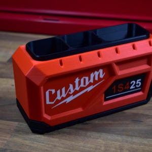 May include: An orange and black custom-made organizer with three compartments. The word "Custom" is printed in white, along with the numbers "1S425". The organizer is made of a durable material and is designed for tools or small items.
