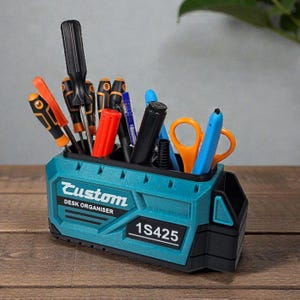 May include: A teal and black desk organizer with the word "Custom" and "DESK ORGANISER" printed on the front. The organizer holds various tools, including screwdrivers, pens, and scissors. The model number "1S425" is also printed on the front.