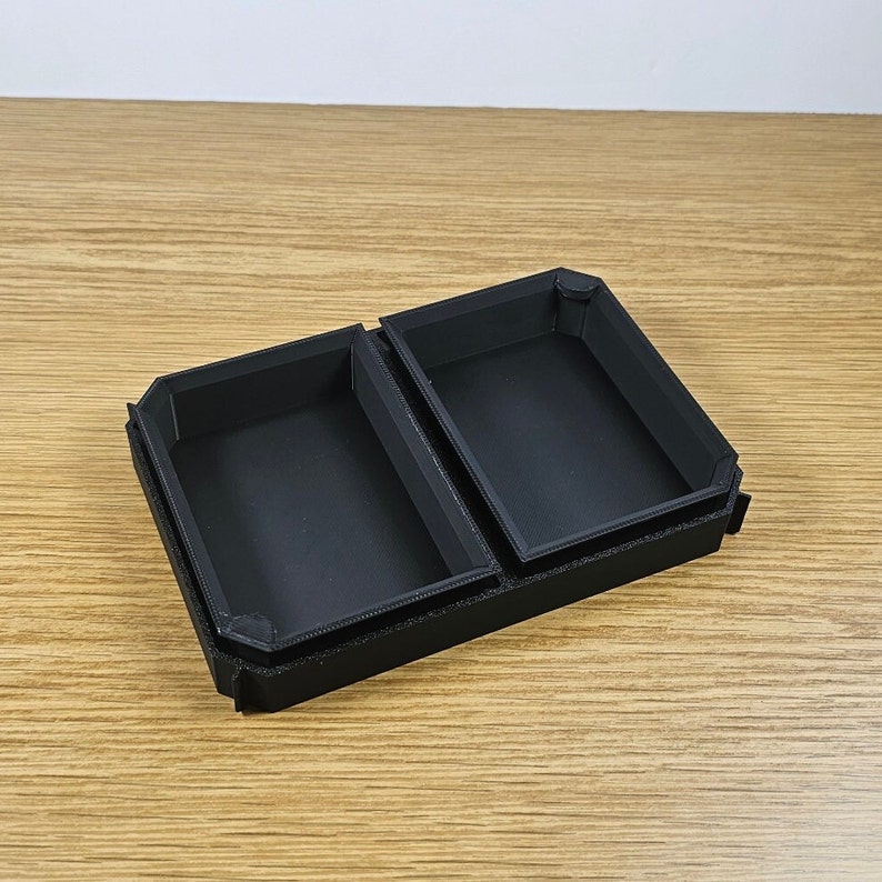 May include: A black plastic box with two compartments, each with a rectangular opening. The box is open and the compartments are visible.