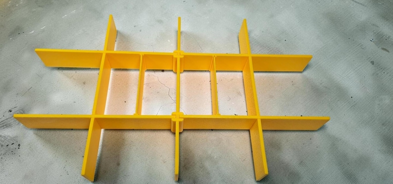May include: Bright yellow plastic grid structure with intersecting horizontal and vertical bars, creating rectangular compartments. The grid is designed for organization and storage, with a simple, functional aesthetic.